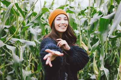 Portrait of smiling young woman gesturing while standing against corns on farm