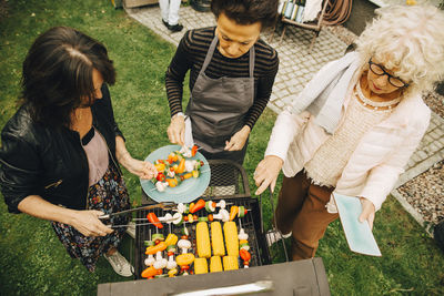 High angle view of elderly female friends barbecuing dinner at back yard during party