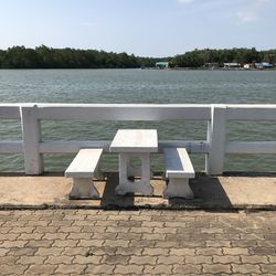 Empty bench by lake against sky