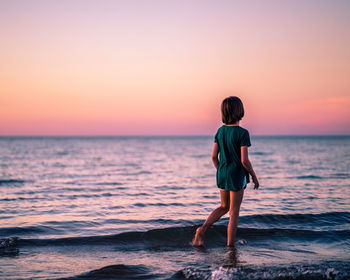 Rear view of boy standing on beach during sunset