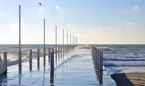 Wooden posts in calm sea against sky