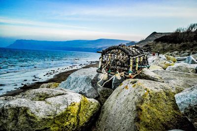 Crab cages on rocks at beach against sky