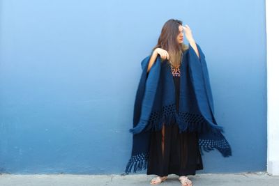 Woman with blanket standing against blue wall