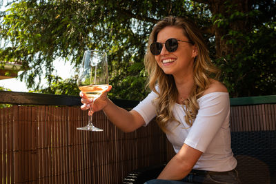 Young woman wearing sunglasses holding wine outdoors