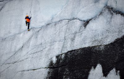 Low angle view of person climbing snow covered rocky mountain
