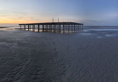 Pier on beach against sky during sunset