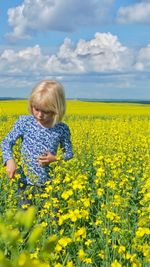 Smiling girl standing amidst yellow flowering plants against sky