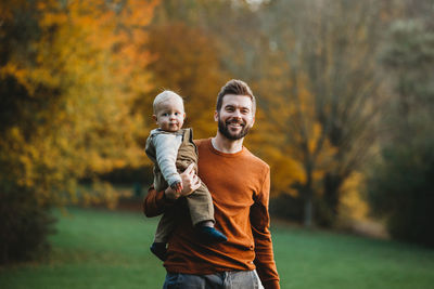 Full length portrait of boy smiling while standing against trees during autumn