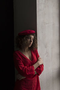 Young woman looking away while standing against wall