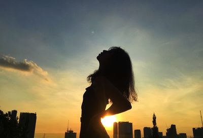 Side view of woman standing against sky during sunset