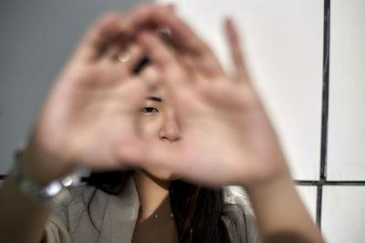 Young woman against wall while looking through hand