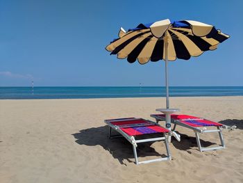 Deck chairs on beach against sky