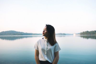 Young woman standing on lakeshore against sky