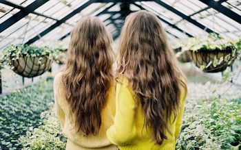 Rear view of sisters standing amidst plants in greenhouse