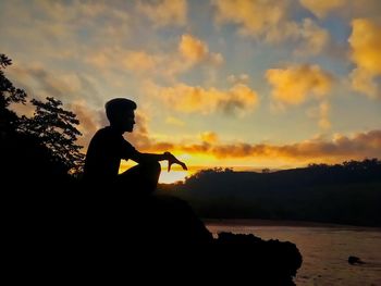 Silhouette man sitting against sky during sunset