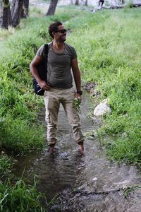 Young man with backpack standing in stream amidst plants