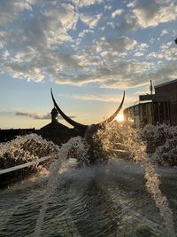 Water splashing on sea by buildings against sky during sunset