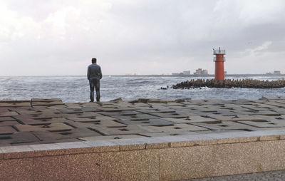 Rear view of man standing on beach against cloudy sky