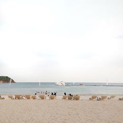 People enjoying by deck chairs at beach against clear sky