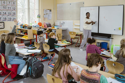 Female teacher talking to male and female pupils during lecture in classroom