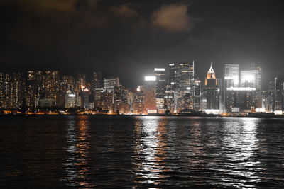 Illuminated buildings by river against sky at night