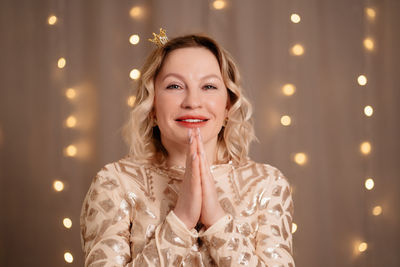 Portrait of beautiful woman with hands clasped against illuminated lighting at home