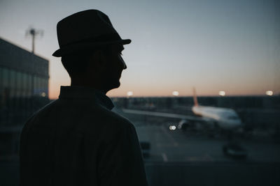 Rear view of man looking at camera against sky during sunset