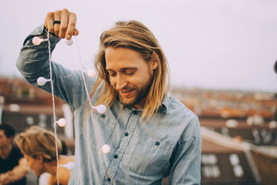 Smiling young man with string light standing on terrace during party