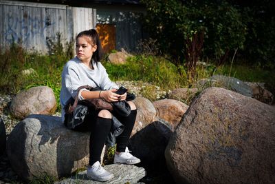 Full length of teenage boy sitting on rock