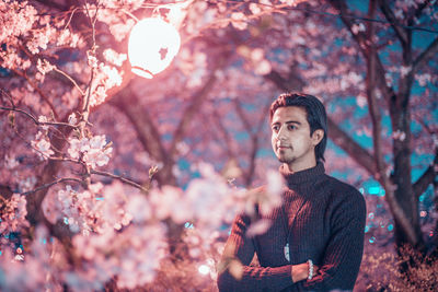 Young man looking away by cherry tree at night