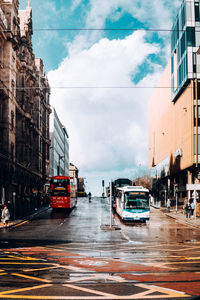 Cars on city street by buildings against sky