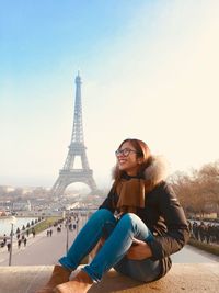 Smiling young woman sitting against eiffel tower in city