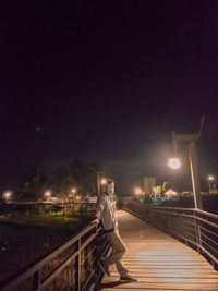 Man standing on illuminated street against sky at night