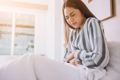 Young woman looking away while sitting on bed