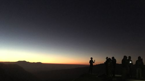 Silhouette friends standing on mountain against clear sky during sunset