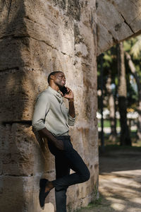 Side view of young man using mobile phone against wall