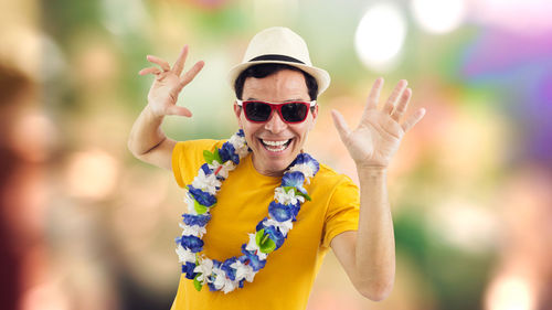 Portrait of excited man wearing sunglasses and floral garland while screaming against colored background