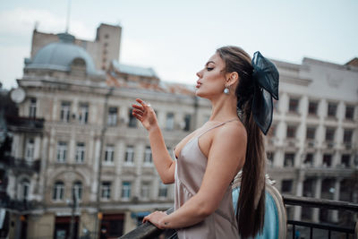 Side view of young woman standing against buildings in city