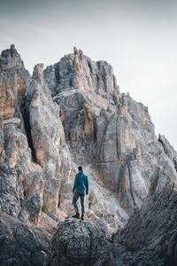 Rear view of man standing on rocky mountain against sky