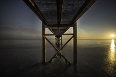 Silhouette pier over sea against sky during sunset