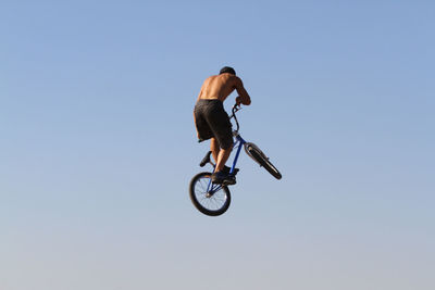 Rear view of cyclist performing stunt in mid-air against clear blue sky