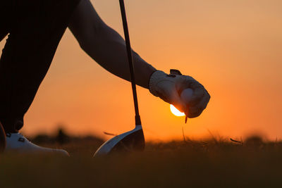 Midsection of man holding umbrella on field against sky during sunset