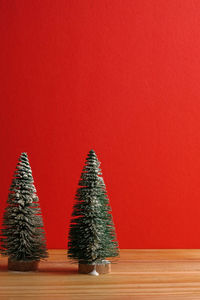 Close-up of small christmas trees on wooden table against red background