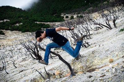 Full length of man with arms outstretched on rock at forest