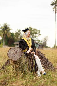 Woman in graduation gown sitting on log