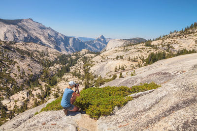 Woman photographing on mountain against clear blue sky