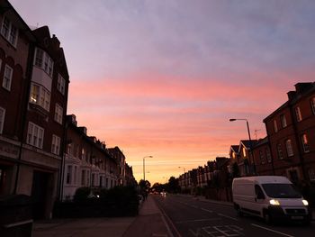 Cars on road amidst buildings against sky during sunset