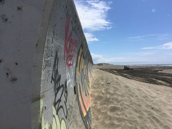 Graffiti on wall by beach against sky