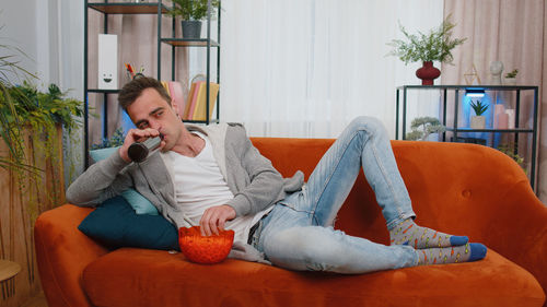 Man with popcorn bowl drinking water on sofa at home
