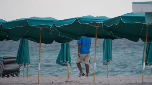 Rear view of man walking by parasols at beach